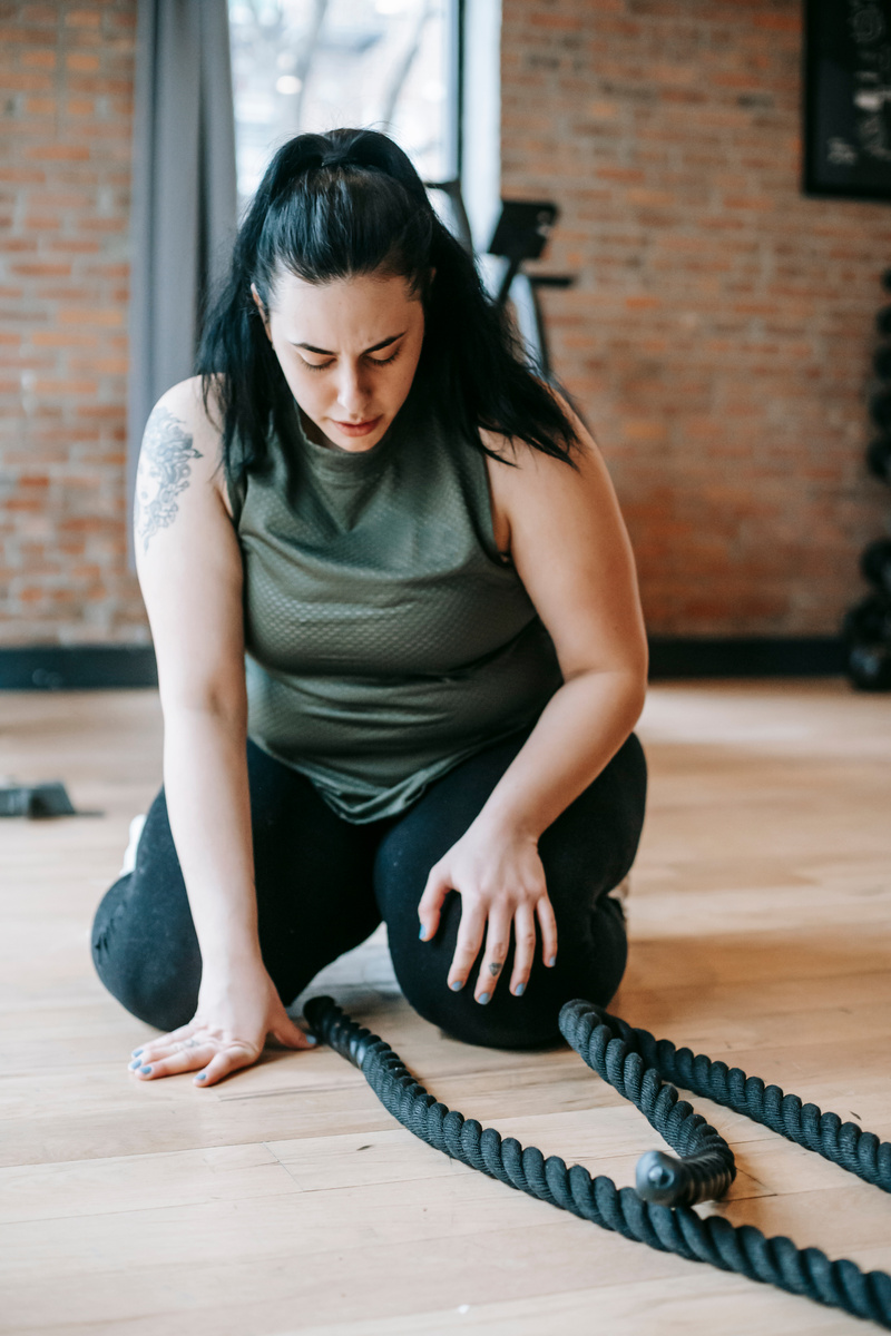 Serious plump sportswoman working out with ropes in gym